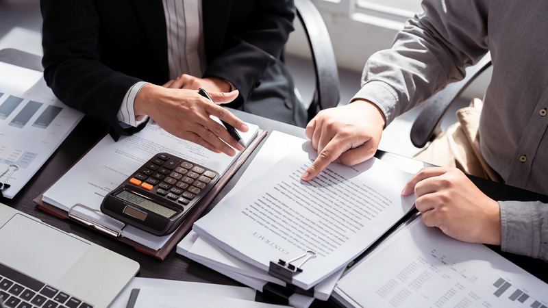 Two professionals reviewing a business sale agreement with a calculator, representing the deal structure analysis provided by Denver investment advisors and financial planners in Colorado.